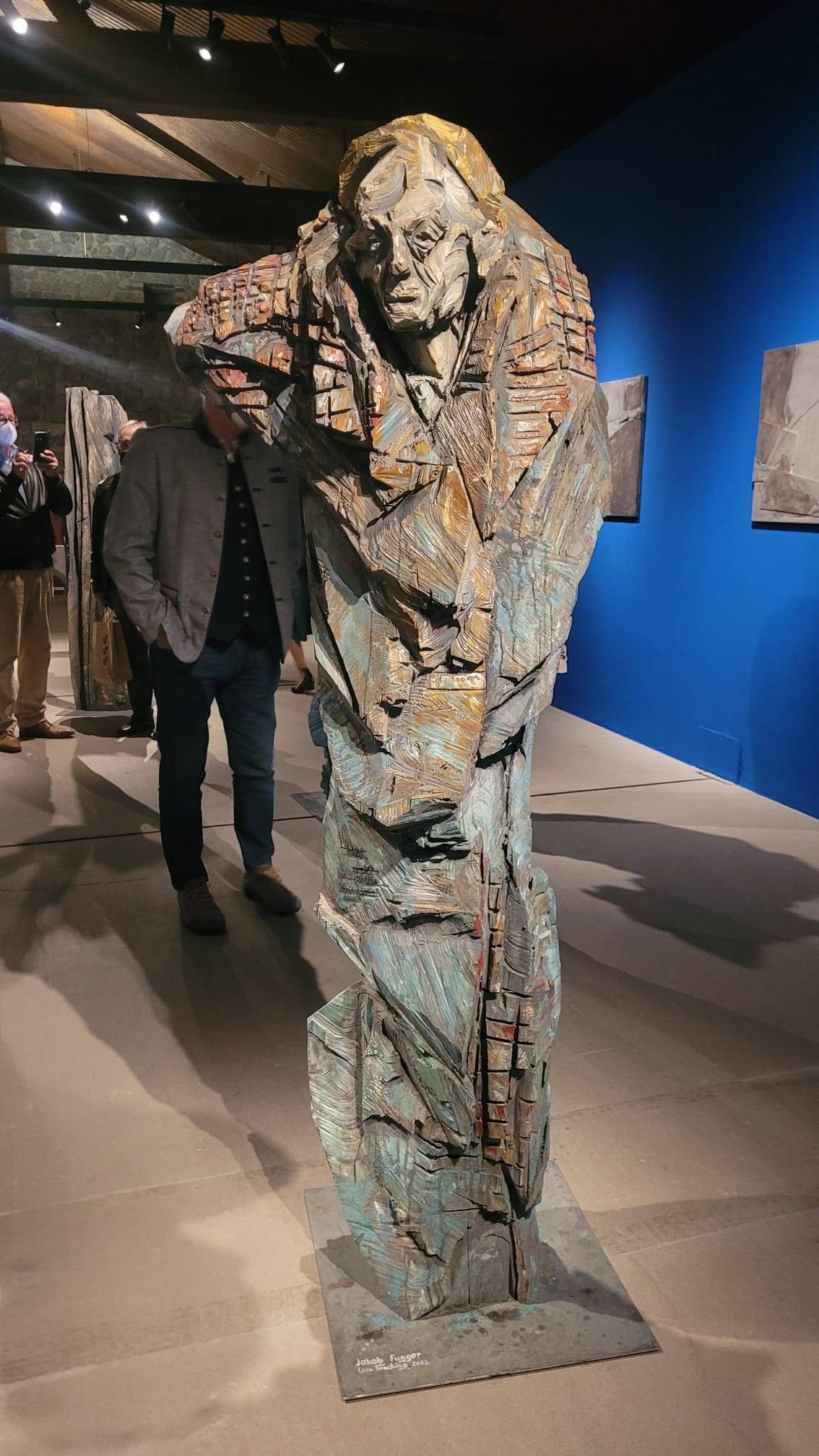 Beleuchtete lebensgroße Holzfigur mit gelber Kappe und blau-grauem Körper und sichtbaren Kettensägespuren